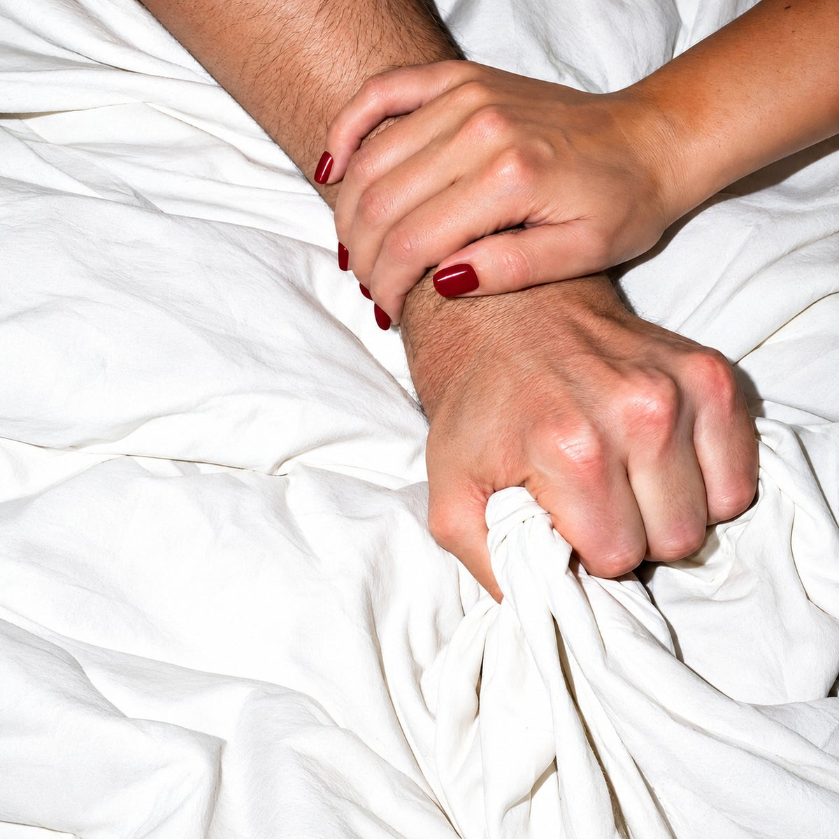 Woman's hand holding a man's wrist as he grips the bed sheets